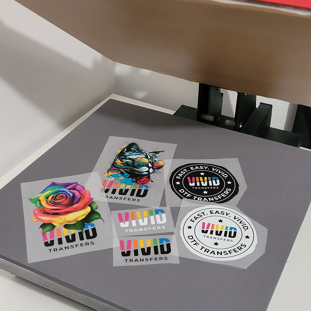A range of DTF Transfers that come in a Vivid Transfers Sample pack all sitting on top of the Heat Press machine